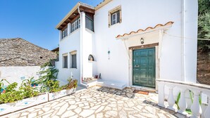 A white building with a green door, stone flooring, and a stone wall. - Holiday Home 'Priest's Traditional Mansion' with Sea View, Shared Terrace and Wi-Fi (Corfu)