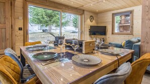 Un intérieur en bois avec une table à manger dressée pour quatre personnes, un canapé et un téléviseur fixé au mur.