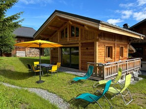 A wooden cabin with a deck, outdoor seating, and a stone wall. - Chalet 'Mazot Savoyard' with Mountain View, Private Terrace and Wi-Fi (Taninges)