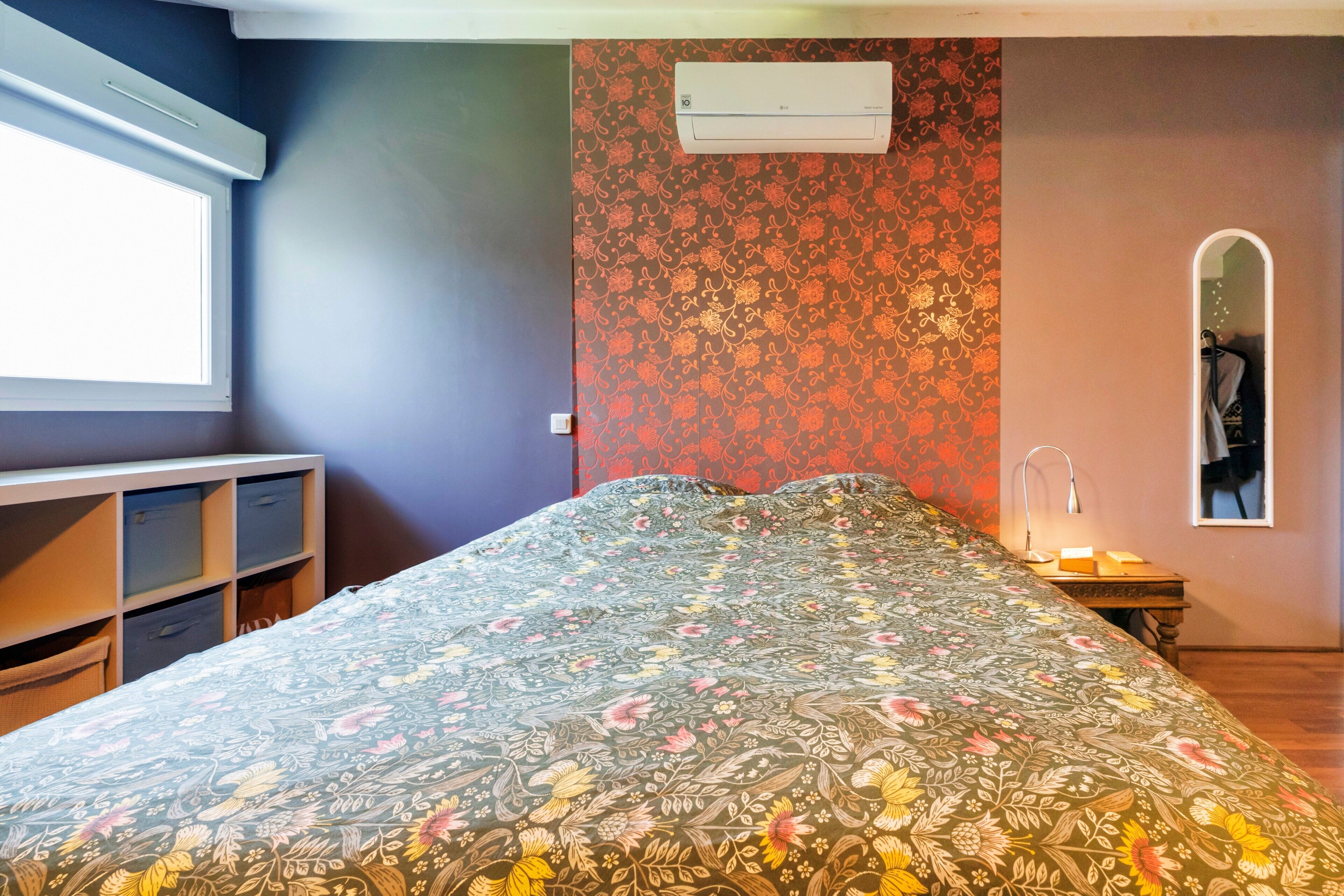 Une chambre à coucher comprenant un lit, une armoire, un appareil de climatisation, un bureau et un miroir.