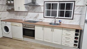 A compact kitchen with a washing machine, oven, and a window above the sink.