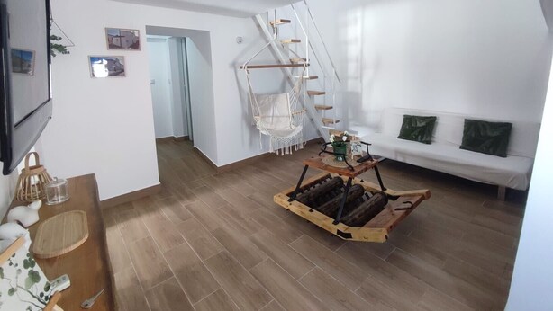 A spacious living area with a white sofa, a wooden coffee table, a hammock, and a staircase.