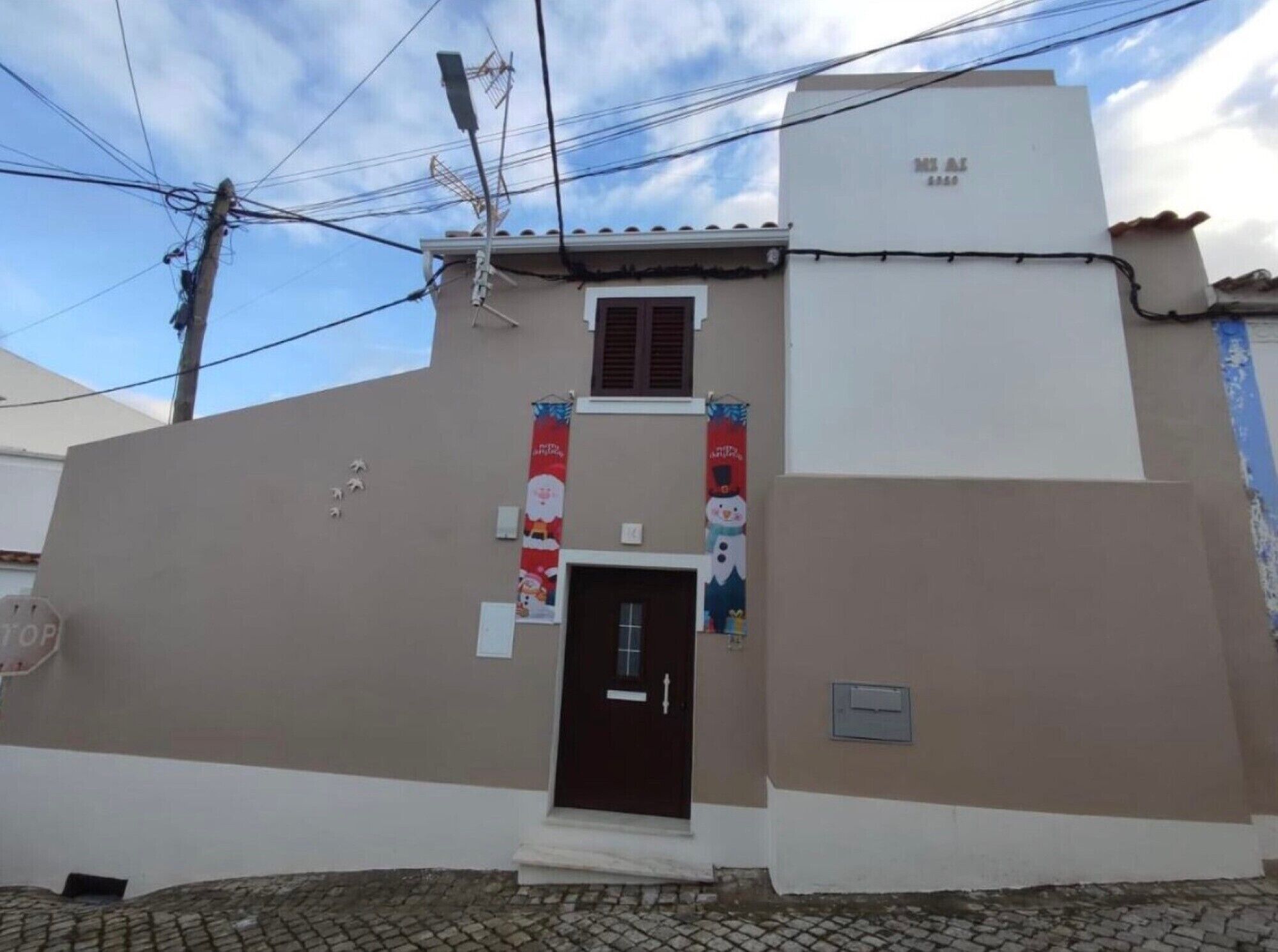 Un bâtiment à la façade marron, avec une porte brun foncé et une petite fenêtre. Deux banderoles sont accrochées au mur, l’une représentant le Père Noël et l’autre un bonhomme de neige.