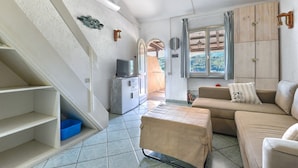 Ein Zimmer mit einer Couch, einem Fernseher, einer Treppe und einem Fenster mit Vorhängen.