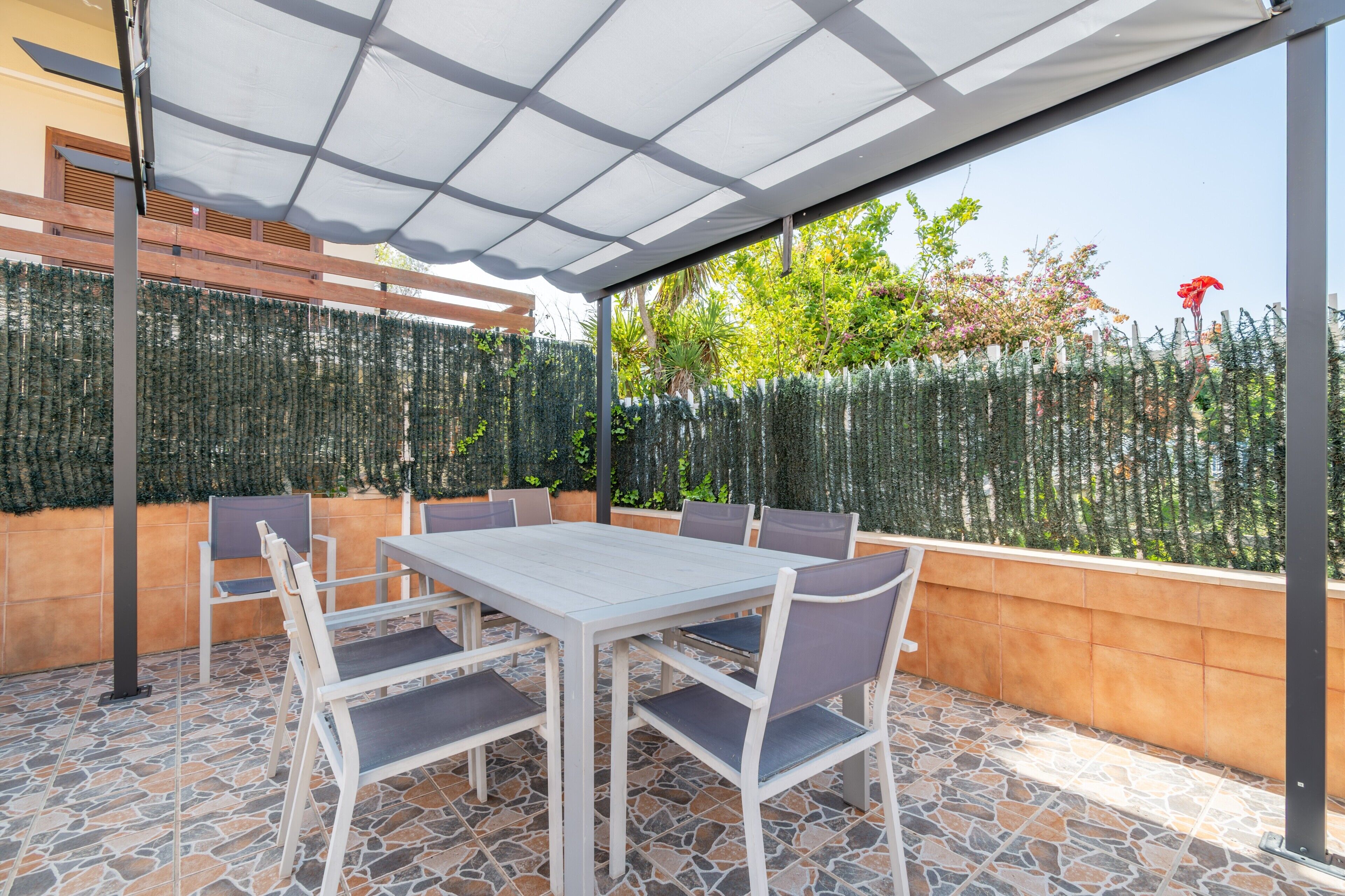 Un patio al aire libre con una mesa, sillas, una pérgola y una cerca decorativa.