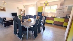 A modern kitchen with a dining area, featuring a large table and chairs, a TV, and a bright yellow and green color scheme. - Villa 'A Suara' with Mountain View, Private Pool and Private Terrace (Canale-di-Verde)