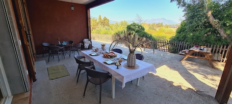 An outdoor dining area with a table set for two, surrounded by chairs, a decorative vase, and a view of a natural landscape.