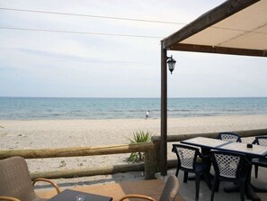 Un restaurant situé en bord de mer, avec une terrasse, une vue sur l’océan et une personne qui se promène sur le sable.