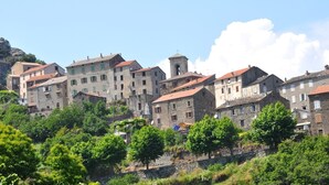 A hillside village with stone buildings, some with red-tiled roofs, and lush greenery in the foreground. - Villa 'Via Ferrata' with Mountain View, Private Pool and Private Terrace (Canale-di-Verde)