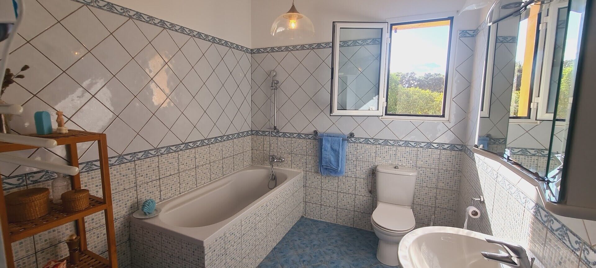 Badeværelse med badekar, toilet og håndvask, udsmykket med mønstrede fliser og et vindue.