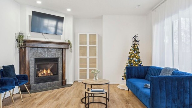 A modern living room with a fireplace, a blue sofa, a Christmas tree, and a flat-screen TV mounted on the wall.