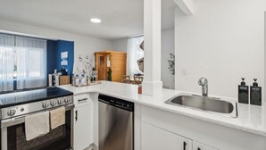 A modern kitchen with white cabinets, a stainless steel sink, and a black stove.