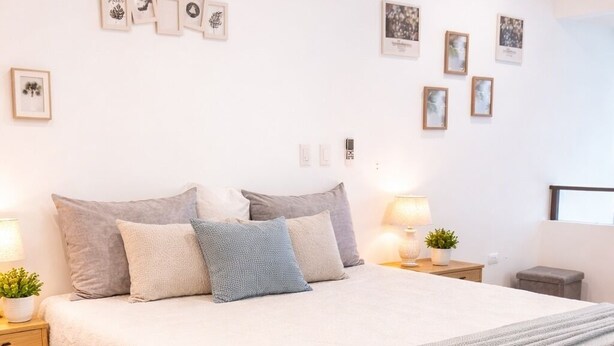 Un dormitorio ordenado con una cama grande, mesitas de noche, una lámpara y cuadros en la pared.