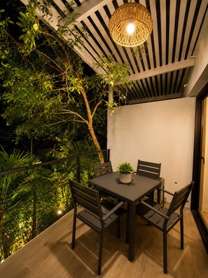 Un área de comedor al aire libre con mesa y sillas, rodeada de follaje y un colgador de luz.