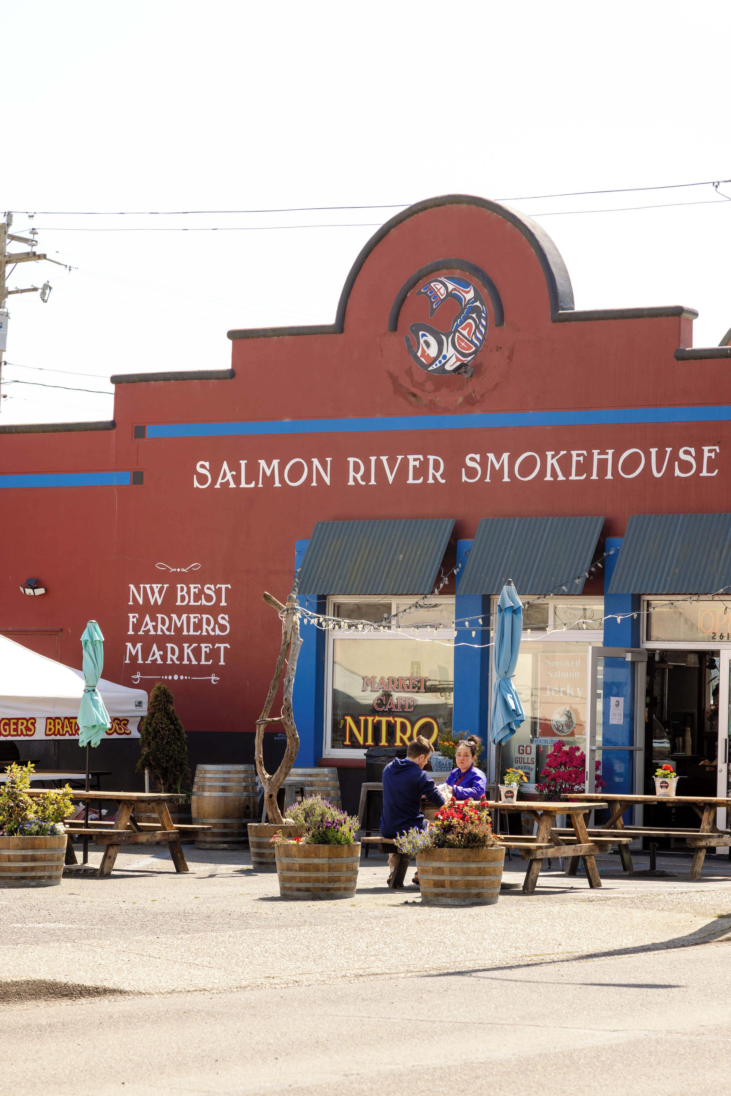 The exterior of the Salmon River Smokehouse, featuring a prominent sign, outdoor seating area, and a market advertisement.