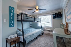 A bunk bed room with a ceiling fan, a window, a TV, and a small table with a sign.