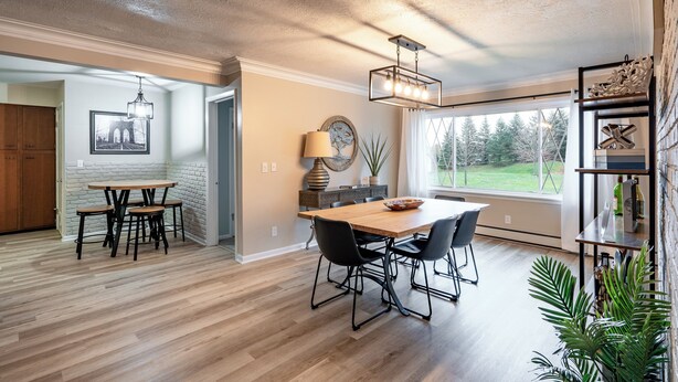 Een ruime eethoek met een houten tafel en stoelen, een hangende lamp en uitzicht op de omgeving door grote ramen.