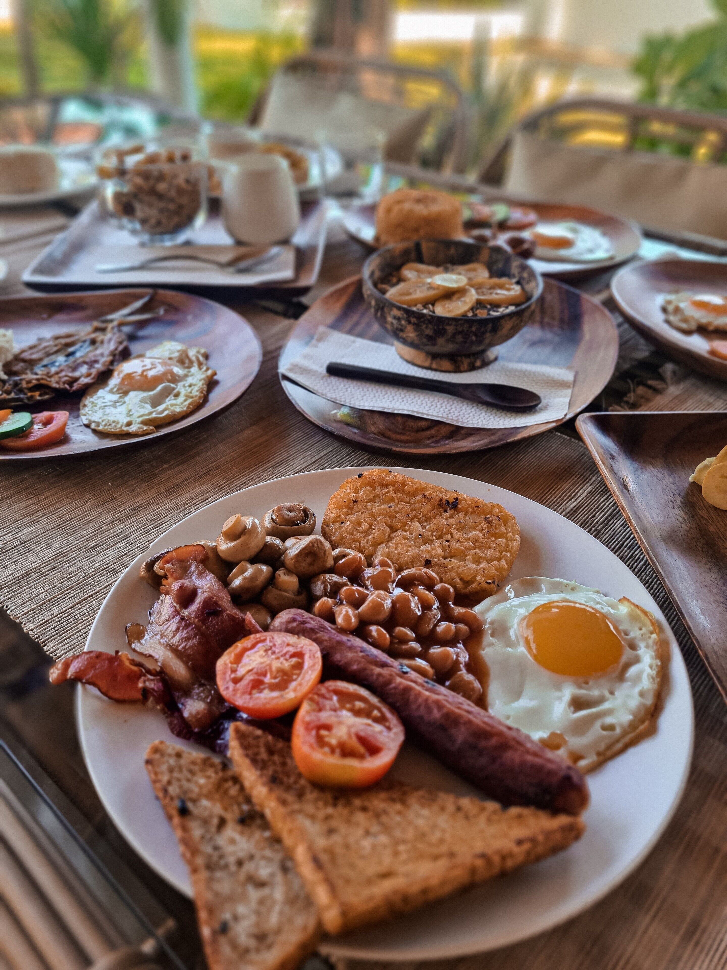 En morgenmadsbuffet med forskellige retter, heriblandt æg, bacon, pølser, bønner og ristet brød.