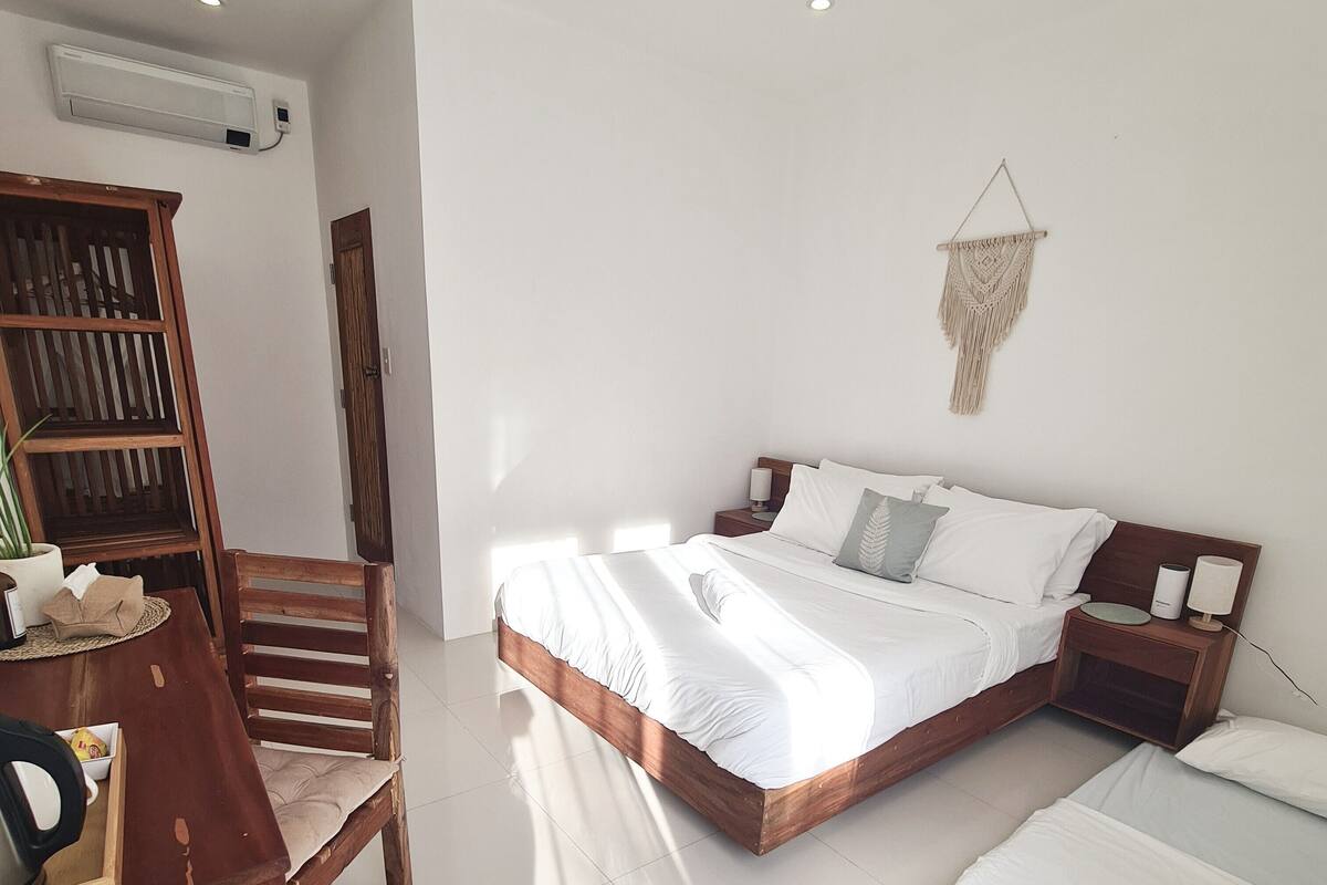 Un dormitorio con una cama, mesitas de noche, una silla de madera, una mesita con una planta y un tapiz de macramé en la pared.