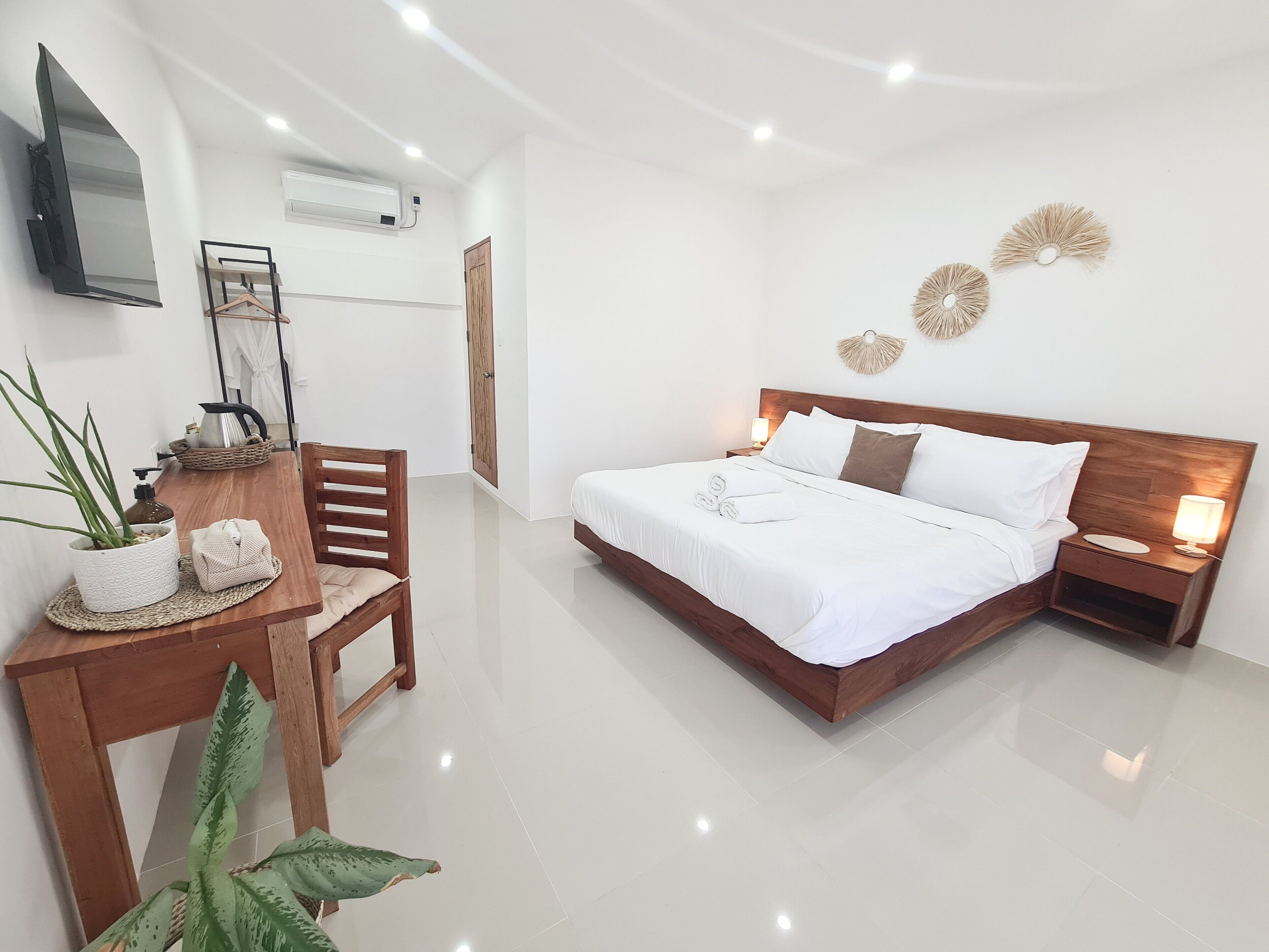 A modern bedroom with a wooden bed, bedside tables, a desk with a chair, a TV, and a wall-mounted air conditioner.