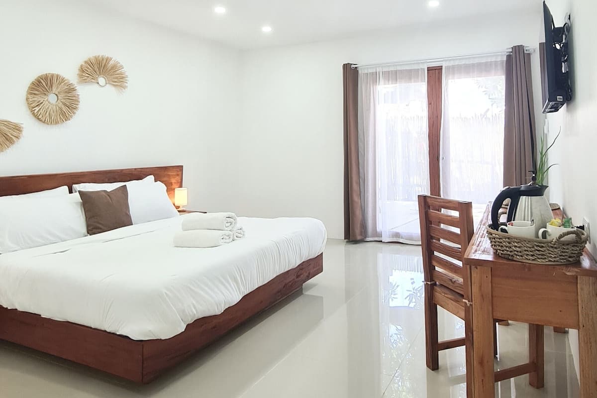 Una habitación de hotel con una cama, una mesa de madera con una tetera, un televisor y una ventana con cortinas.