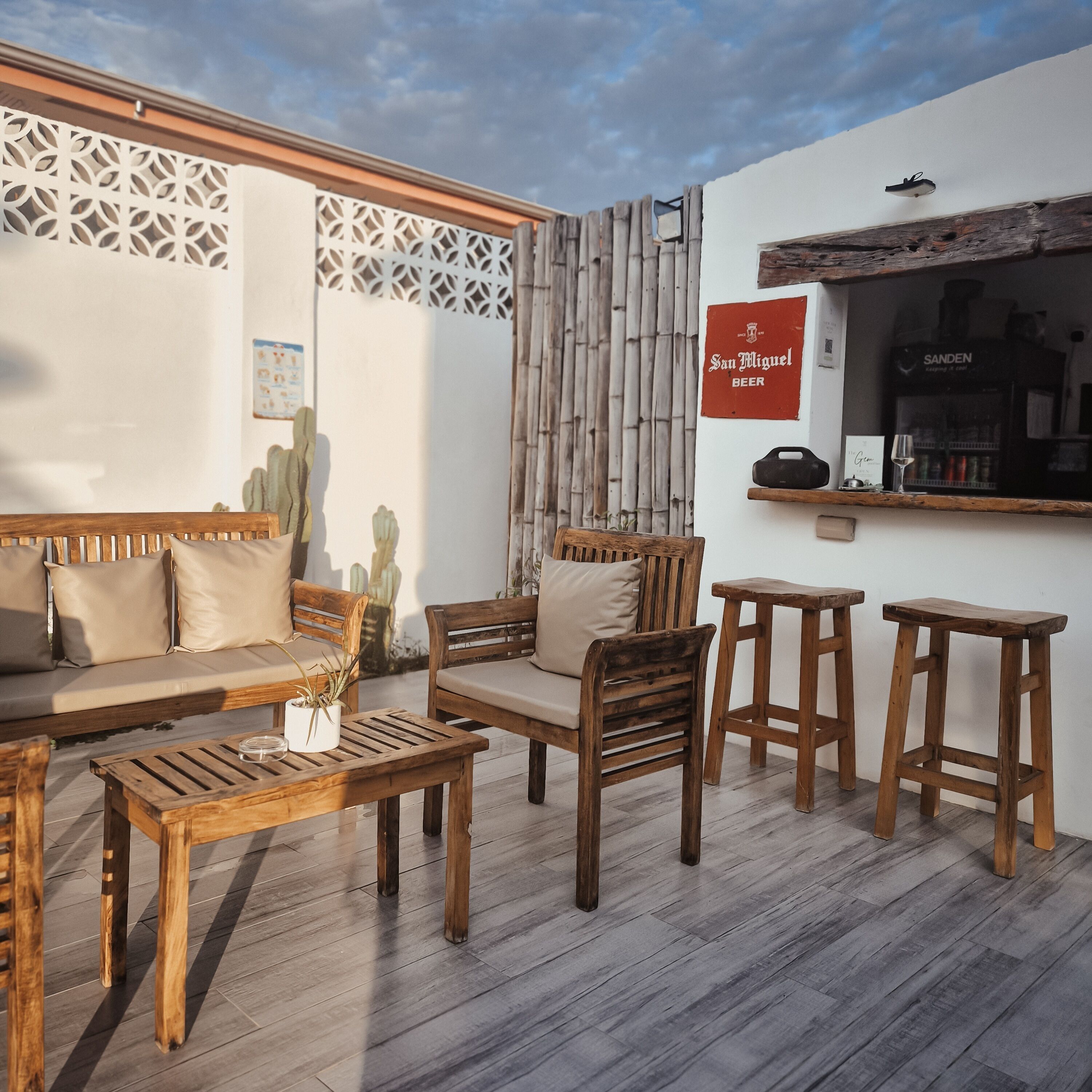 A cozy outdoor seating area with wooden furniture, a cactus plant, and a bar counter with a beer sign.