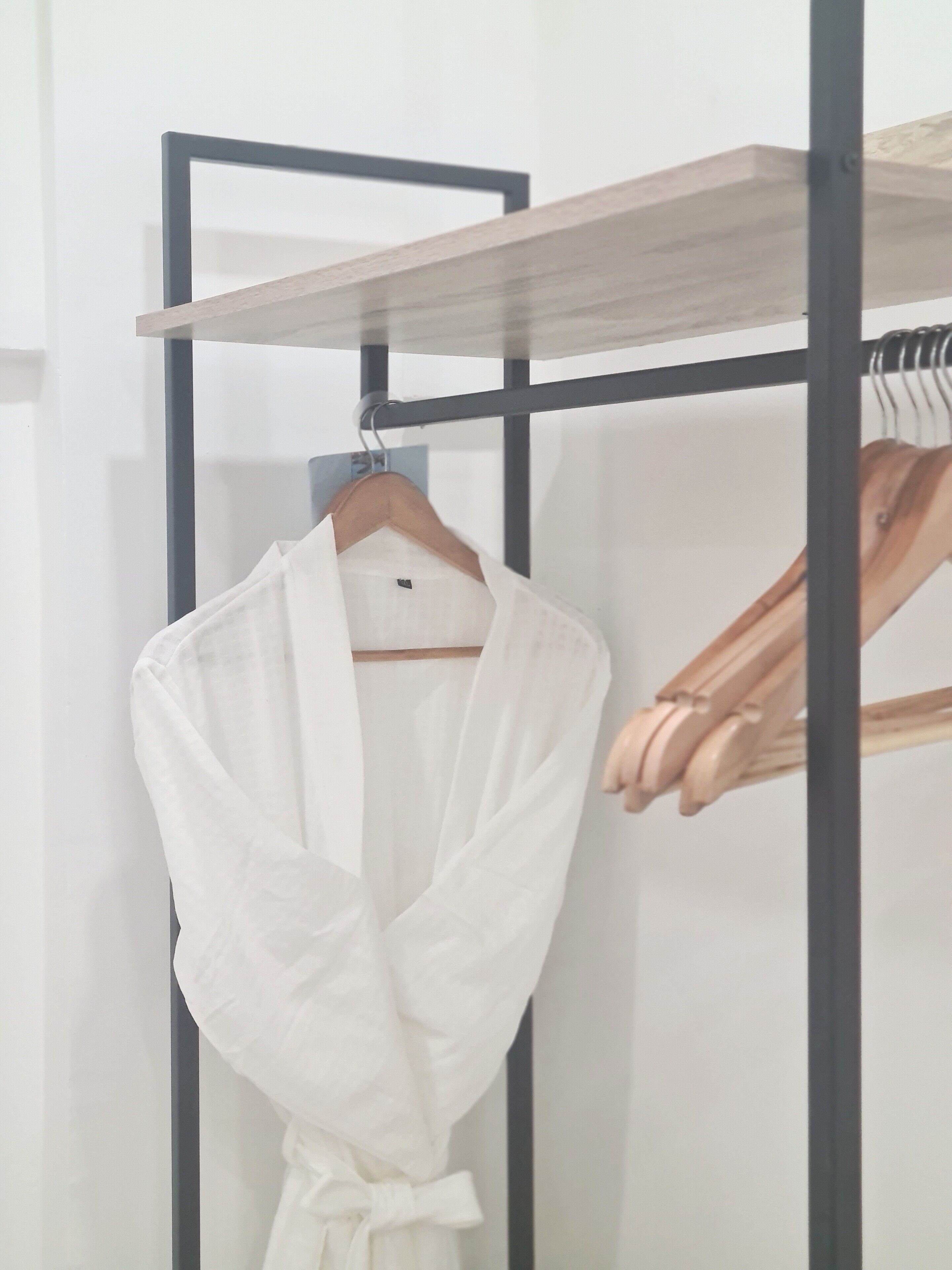 Une blouse blanche est suspendue à un portant métallique, au-dessus duquel se trouve une étagère en bois.