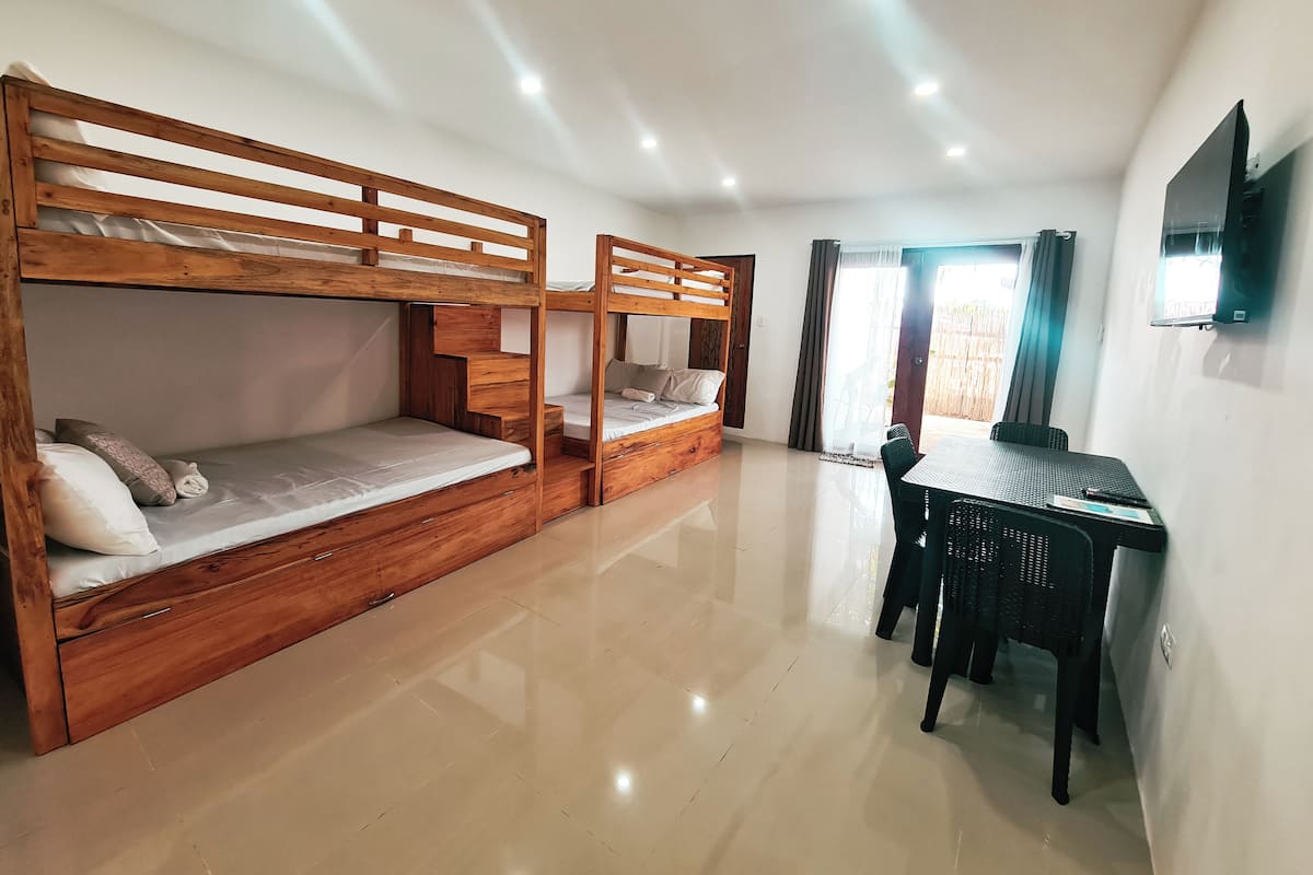 Una habitación con dos literas de madera, un escritorio pequeño con silla, un televisor de pantalla plana en la pared y una puerta corrediza de vidrio que da a un área exterior.