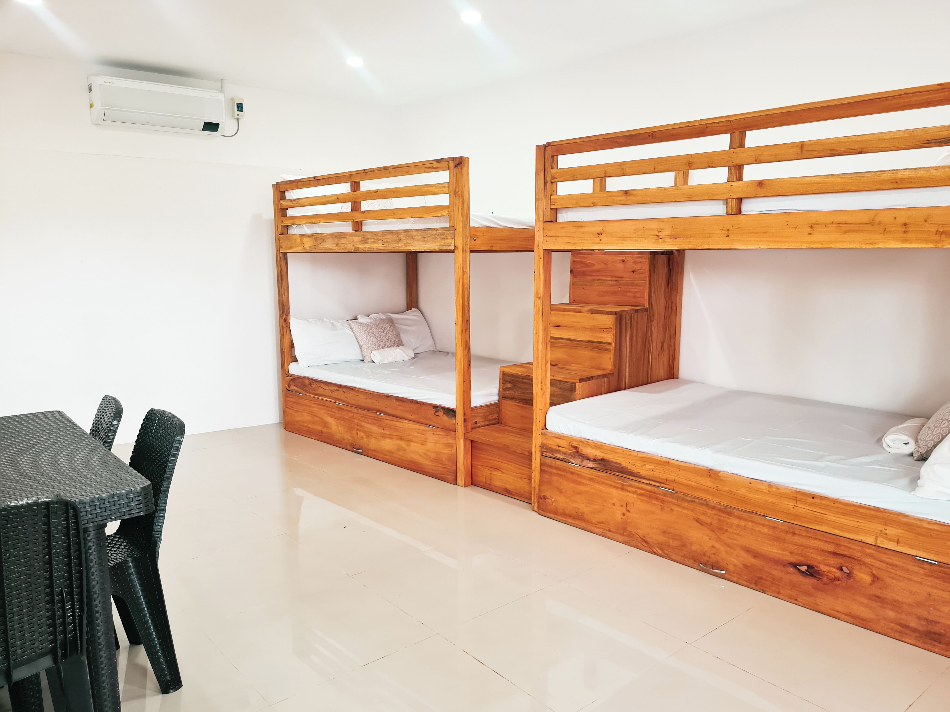 A room with two bunk beds, a small table with chairs, and a wall-mounted air conditioner.