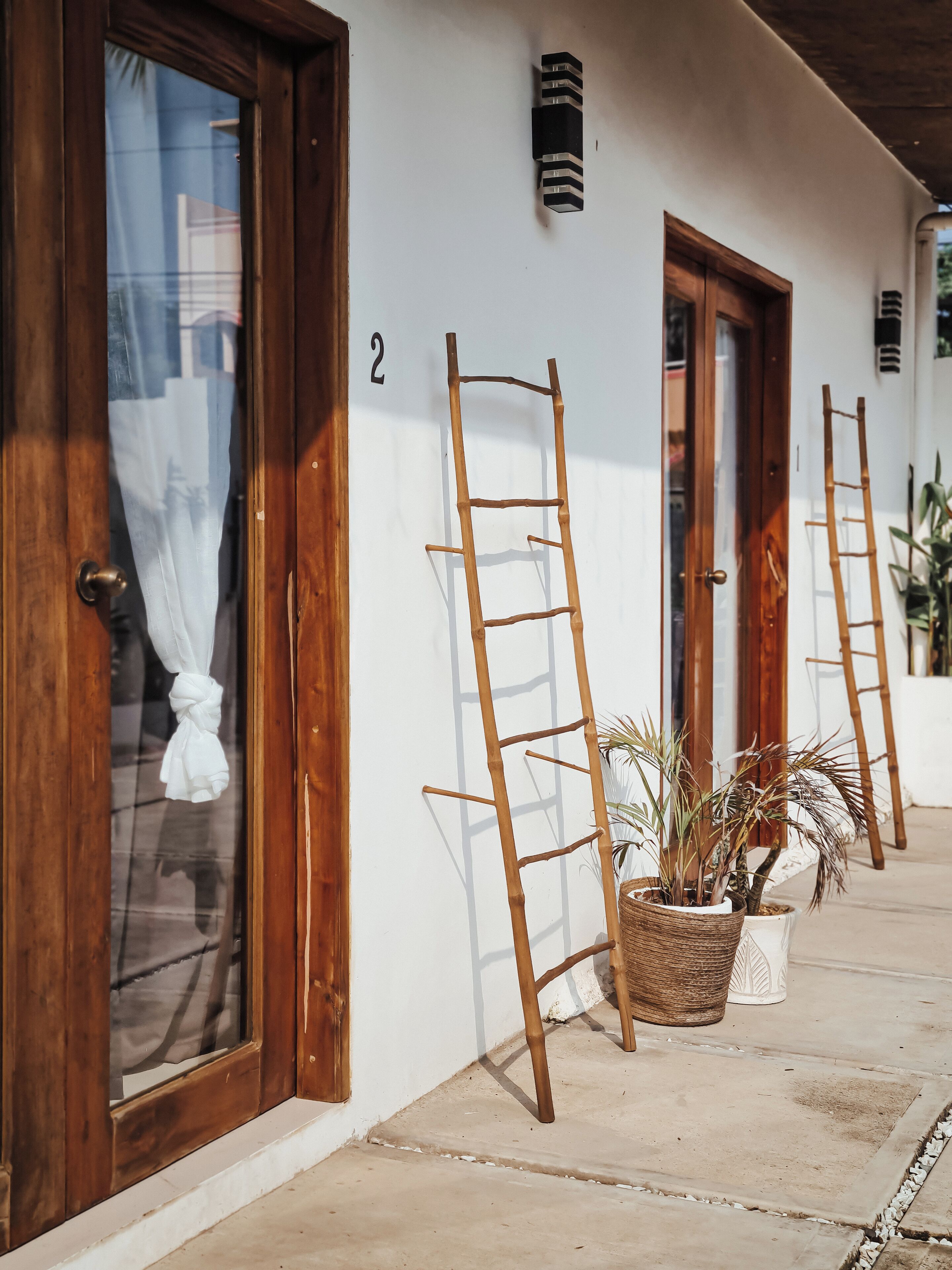 Un bâtiment avec des portes en bois et le chiffre « 2 » peint sur le mur. Deux échelles en bois sont appuyées contre le mur, et un pot de fleurs avec un panier tressé se trouve à proximité.
