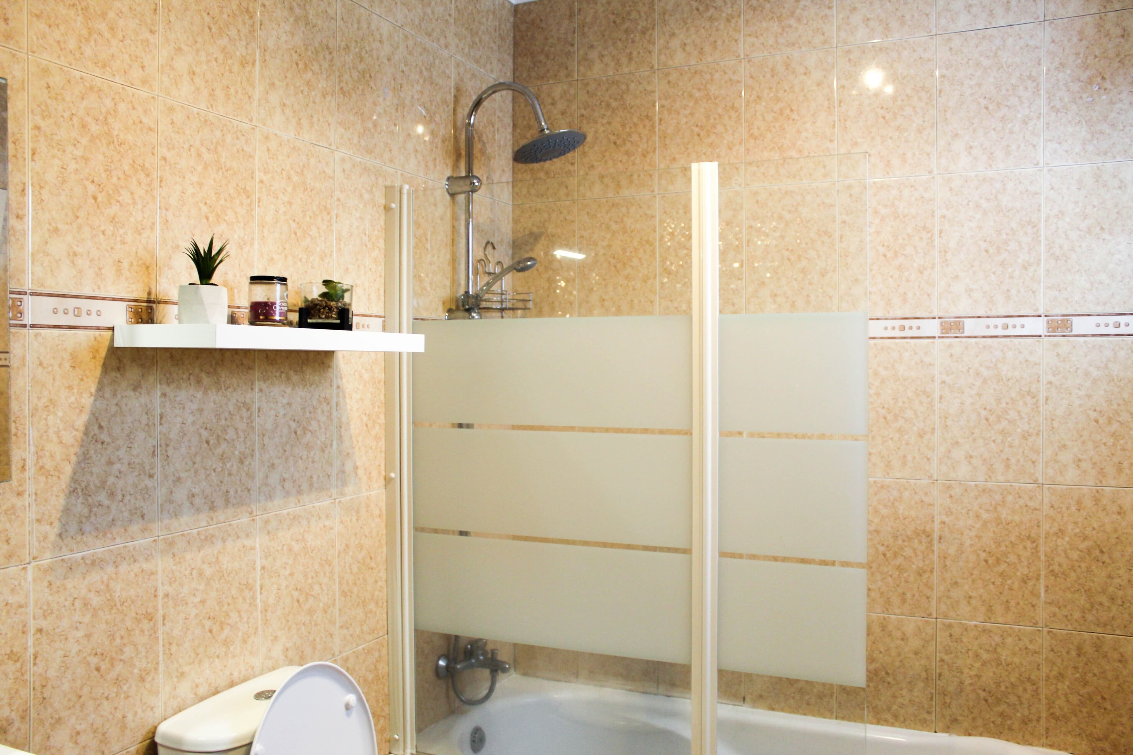 A bathroom with a shower, toilet, and a shelf with toiletries.