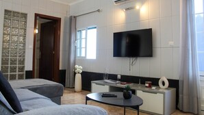 A modern living room with a sofa, a coffee table, a TV mounted on the wall, and a window with curtains. - House 37North (Ponta Delgada)