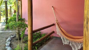 A covered outdoor area with a hammock, a pink wall, and a concrete path. - Pousada In Paradiso (Aracruz)