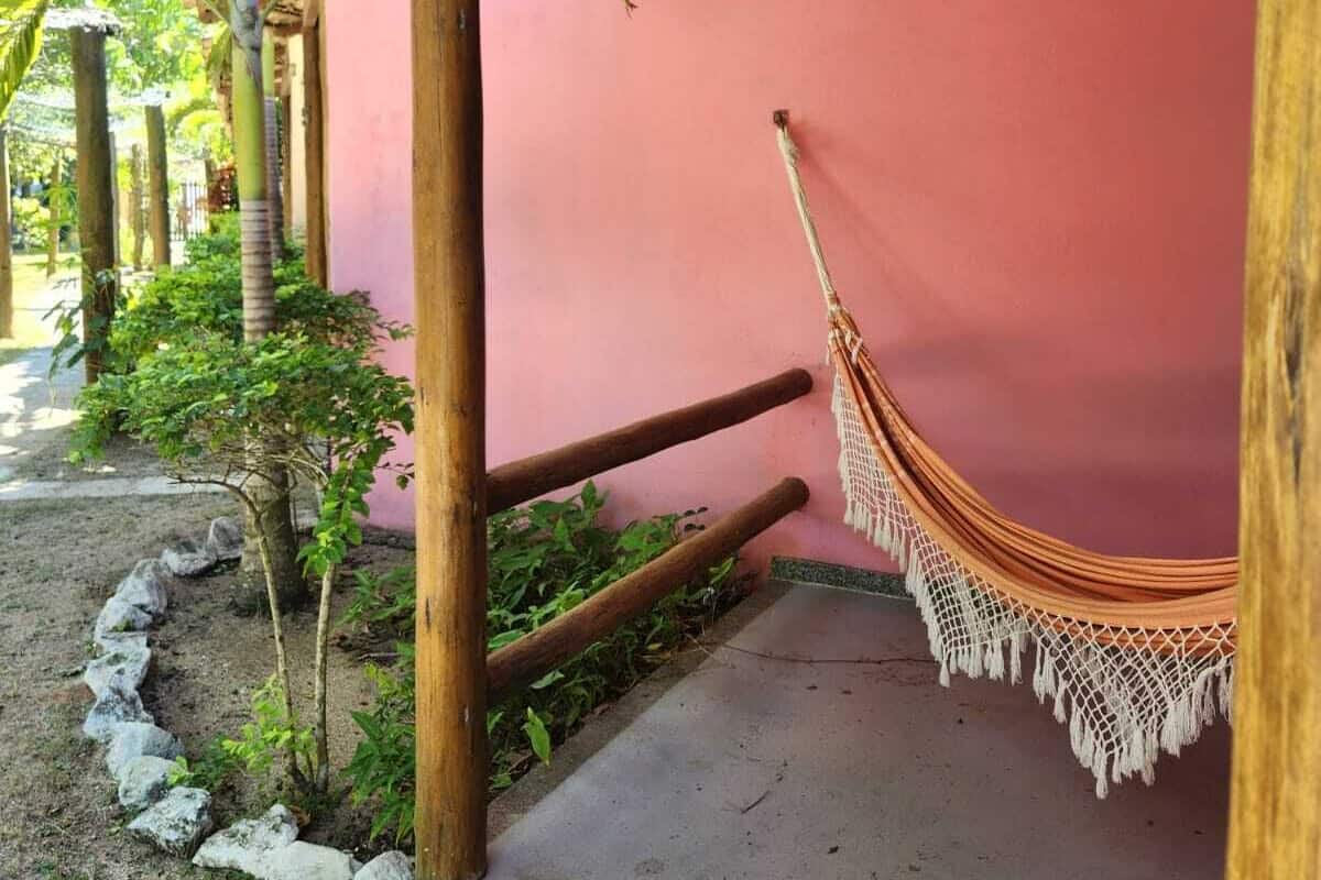 A covered outdoor area with a hammock, a pink wall, and a concrete path.