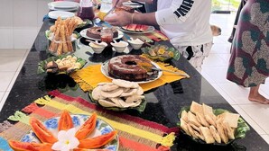 A kitchen with a long counter filled with various food items and a person preparing food. - Pousada In Paradiso (Aracruz)