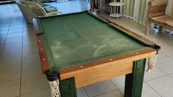 Uma mesa de bilhar numa sala com vista para a área da piscina lá fora.