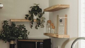 A modern kitchen with a microwave, sink, and wooden shelves.