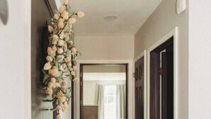 A hallway with wooden flooring, a decorative floral arrangement on the left, and a door on the right.
