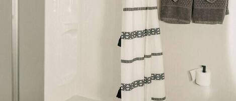 Un baño con cortina de ducha, inodoro y toallas colgadas en un perchero.