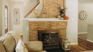 A living room with a brick fireplace, a sofa, and a decorative wall clock.