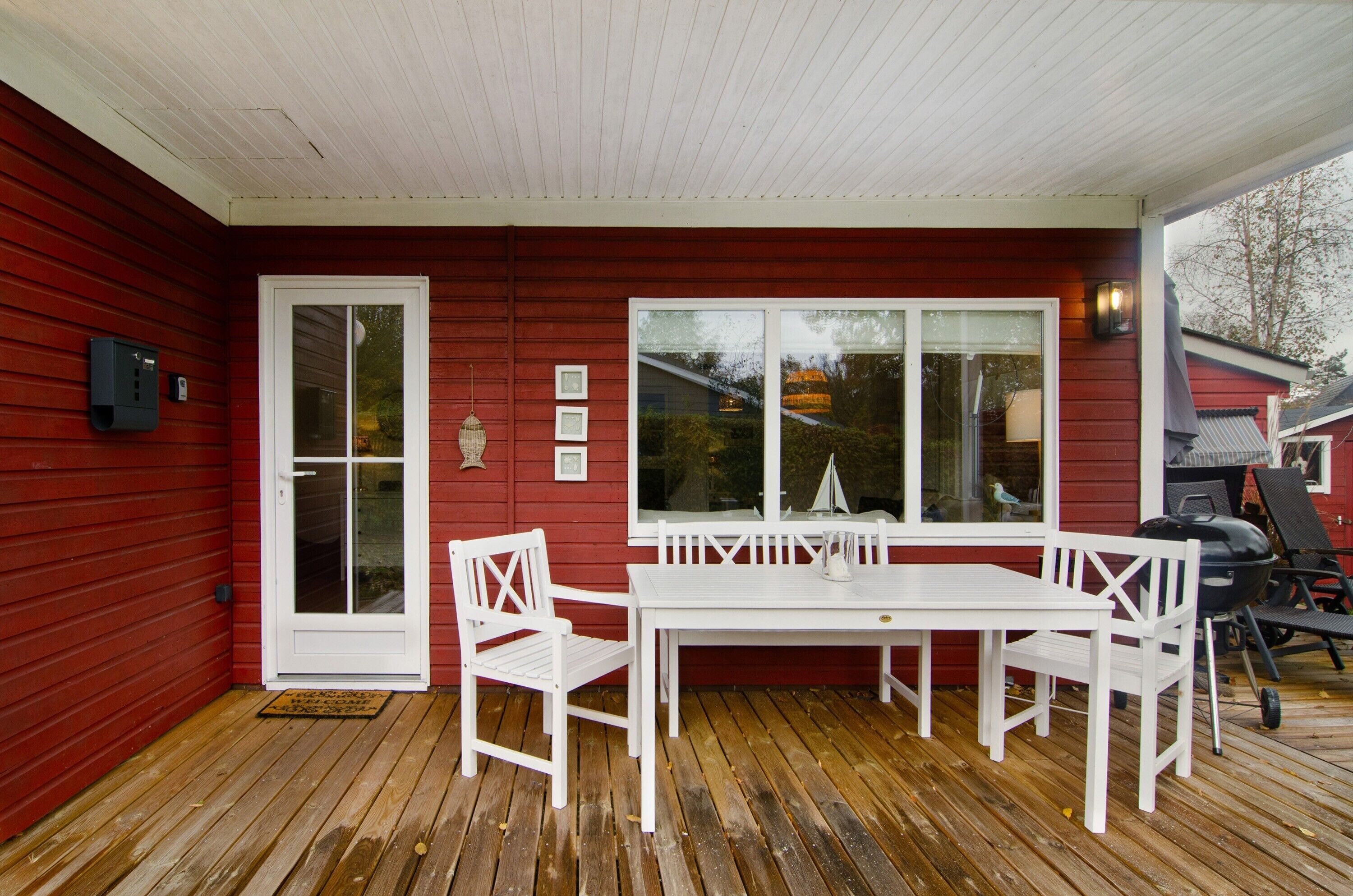 A red wooden house with a white door, a white table with chairs, and a large window.