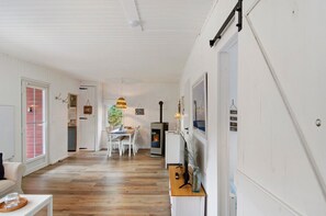 Una habitación amplia con piso de madera, paredes blancas, un área de comedor con mesa y sillas, una pequeña cocina y una chimenea.