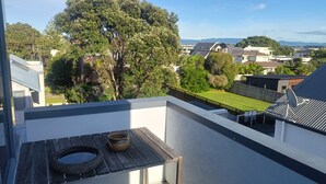 A balcony with a rustic table, a view of a residential area, and a large tree. - Best position in Mt Maunganui, quiet yet central. 300 m from beach & Pilot Bay (Mount Maunganui)