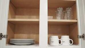 A cabinet with two shelves; the top shelf holds stacked plates, and the bottom shelf has two white coffee mugs with handles.