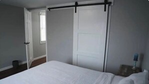 A bedroom with a bed, a white door, and a window.