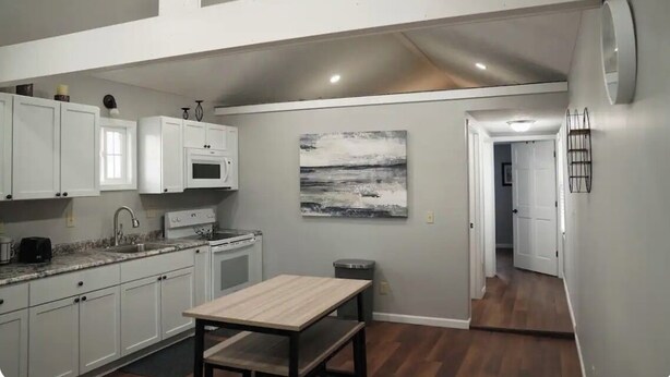 A kitchen with white cabinets, a granite countertop, a wooden table, and a painting on the wall.