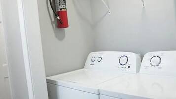 Une buanderie équipée de deux machines à laver blanches, d’un extincteur et d’une étagère en métal.