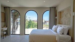 Une chambre d’hôtel avec un grand lit, un bureau et une vue sur l’extérieur grâce à de grandes fenêtres en arc de cercle.