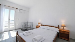 Ein Schlafzimmer mit einem Bett, zwei Nachttischen mit Lampen, einer gläsernen Wendeltreppe und einem großen Fenster mit Vorhängen.