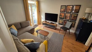 En moderne stue med sofa, sofabord, fjernsyn og bybilleder i rammer på væggen.